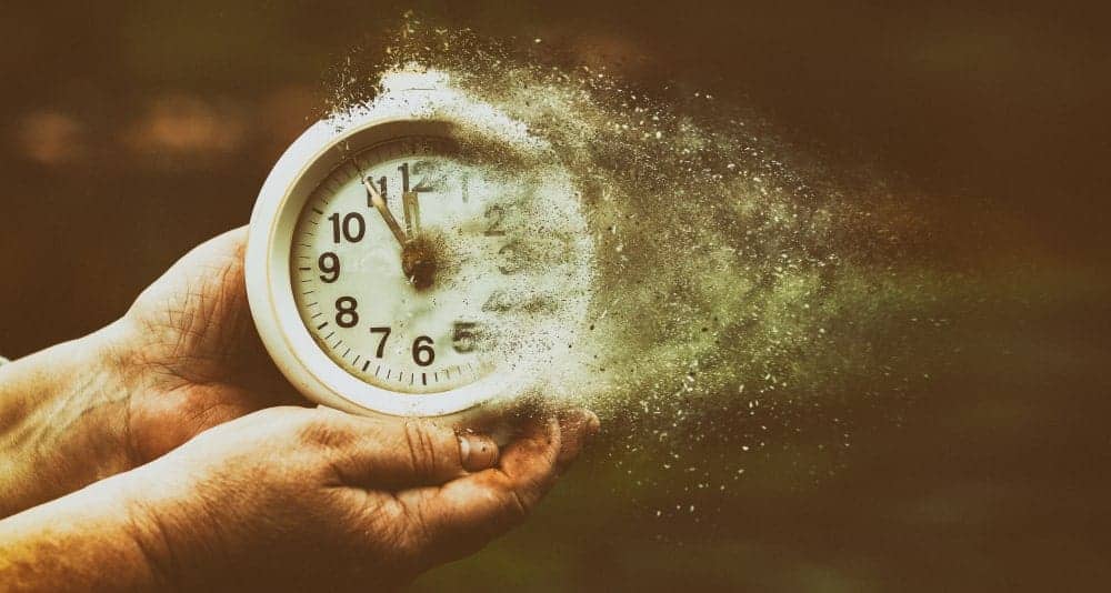 Metaphor for time as it flies by illustrated with hands holding a clock that's turning into dust.