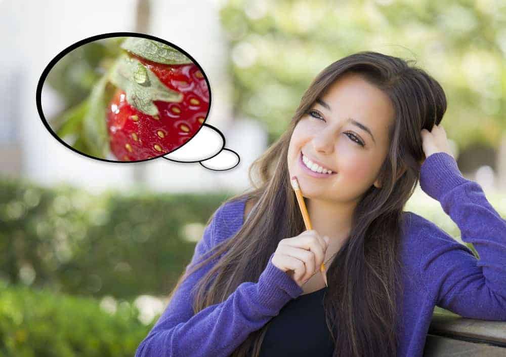 Thinking woman with a pencil on her chin and a bubble head on the side with strawberry photo.