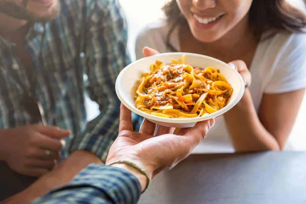 A woman fetching the man's plate of pasta.