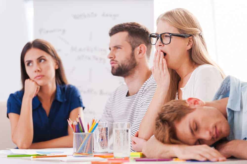 A group of bored people where one is yawning and the other is sleeping.