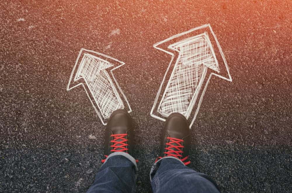 Sneakers standing on two drawn arrows  on an asphalt road pointing to different directions.