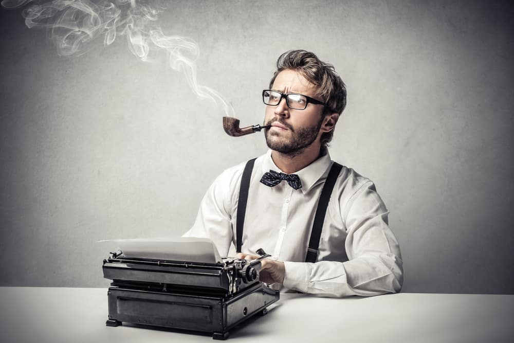 Writer with a tobacco pauses to think with hands on a typewriter.