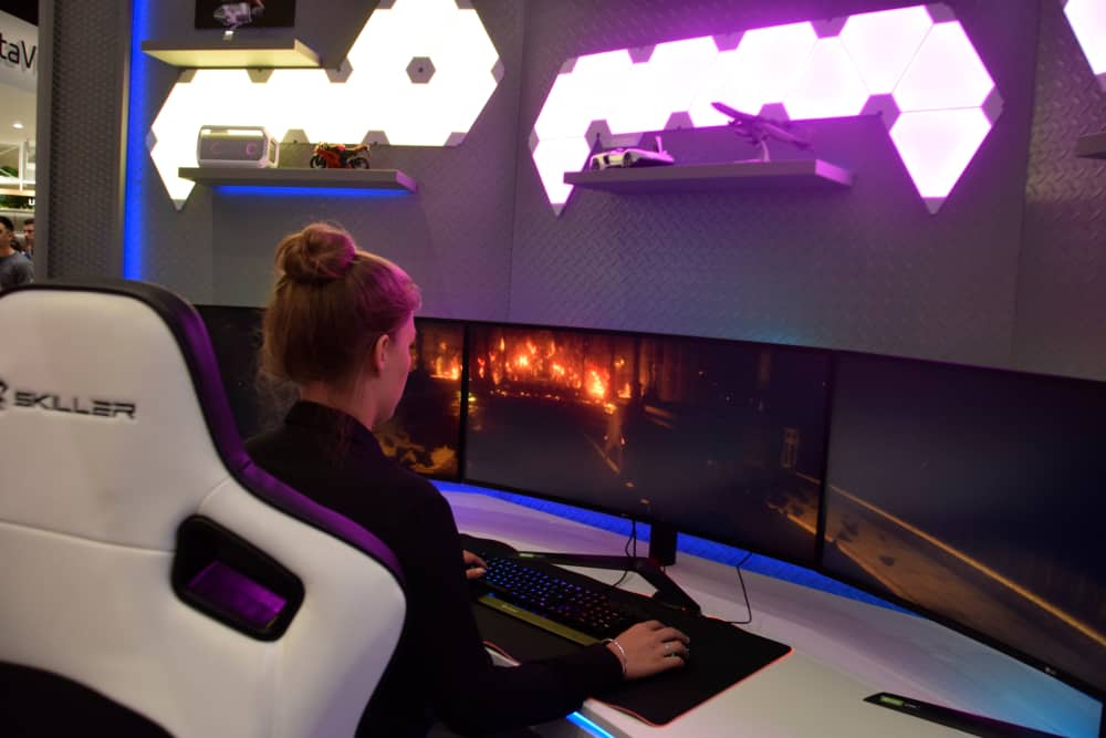 Back view of a woman sitting in front a work desk with three curved computer monitors.